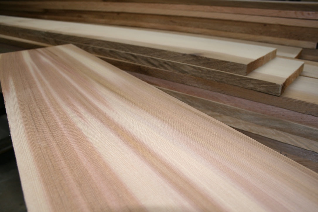 Wide clear old-growth Western Red Cedar board with additional milled cedar lumber in the workshop