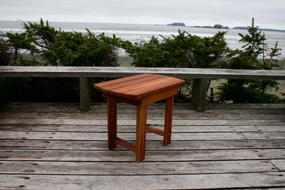 Angled view of the matching side table showing the slatted top, legs and lower support rails on a coastal deck
