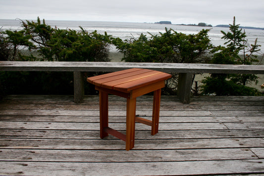 Angled view of the matching side table showing the slatted top, legs and lower support rails on a coastal deck