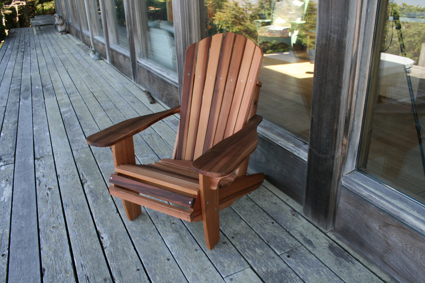 A Cedar Adirondack chair with a natural wood finish, featuring a wide seat and oversized arms, placed on a wooden deck.