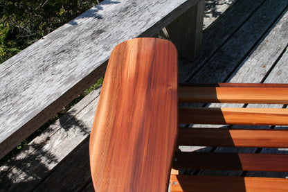 Wide chair arm with rounded edges beside the curved seat slats and stainless-steel fasteners